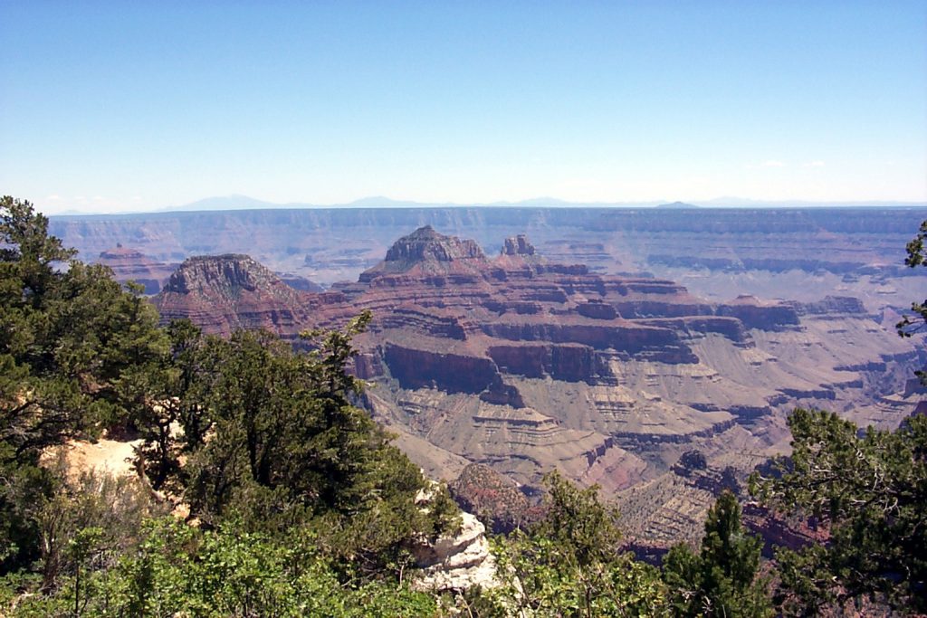 This photo looks out from near the North Rim Lodge and looks straight south. The San Francisco mountains are visible on the horizon. Flagstaff is just south of these mountains. The North Kaibab trail runs down into the valley running from lower centre up and to the right.