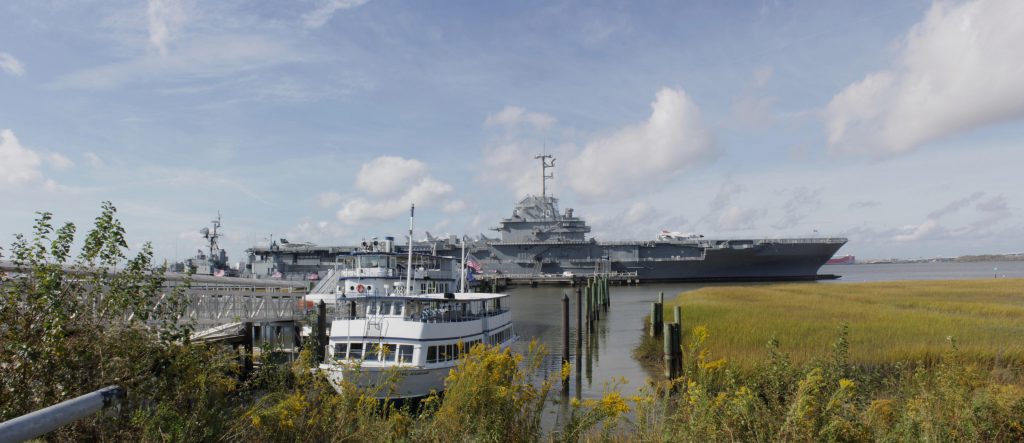 The ferry to Fort Sumter in the foreground at the loading deck with the Yorktown in the background.