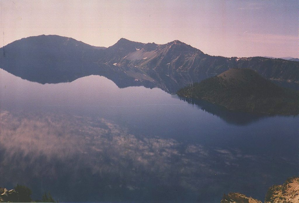 A photo taken from the north rim shows how incredibly smooth the lake can become. Note Wizard Island to the right, but note that the 'mist' on the lake is actually the reflection of the clouds in the sky!